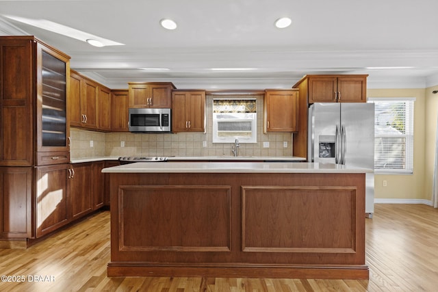 kitchen featuring a center island, light countertops, appliances with stainless steel finishes, brown cabinetry, and a sink