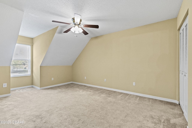 additional living space with lofted ceiling, light colored carpet, ceiling fan, a textured ceiling, and baseboards