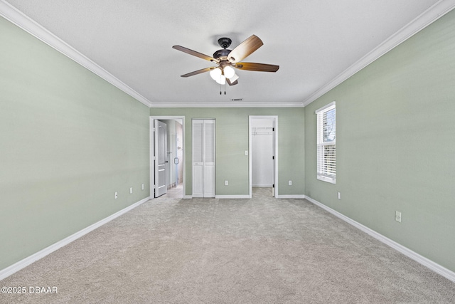 unfurnished bedroom featuring light carpet, a ceiling fan, baseboards, ornamental molding, and ensuite bath