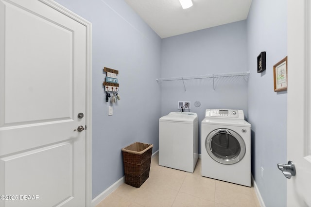 clothes washing area featuring light tile patterned flooring, laundry area, washer and dryer, and baseboards