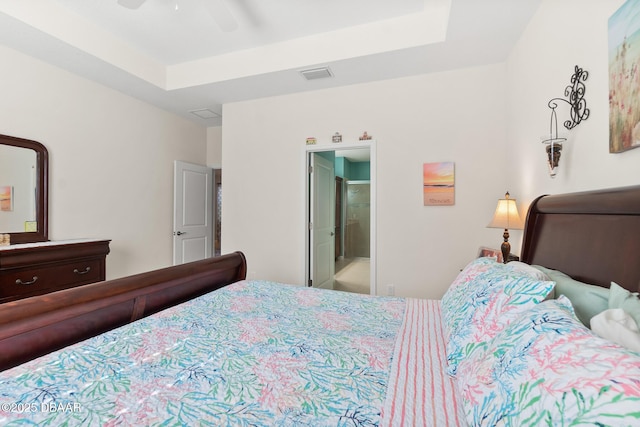 bedroom featuring a tray ceiling, a ceiling fan, visible vents, and ensuite bathroom