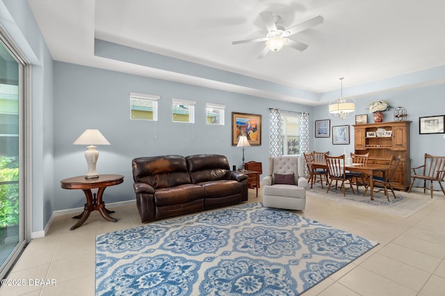 living room with light tile patterned floors, baseboards, a raised ceiling, and ceiling fan