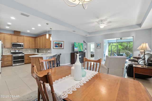 dining room featuring a raised ceiling, light tile patterned floors, a ceiling fan, and visible vents