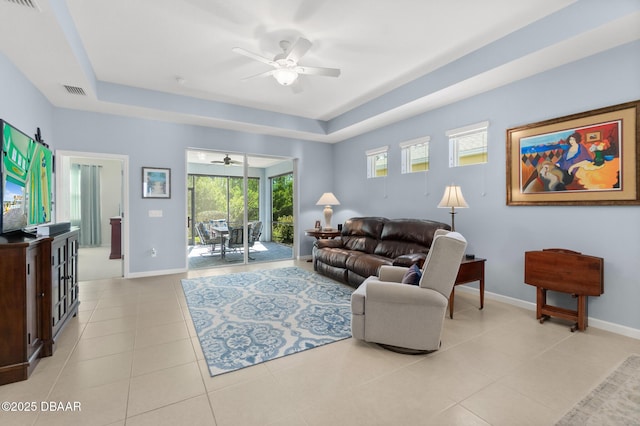 living room with light tile patterned floors, baseboards, a raised ceiling, and a ceiling fan