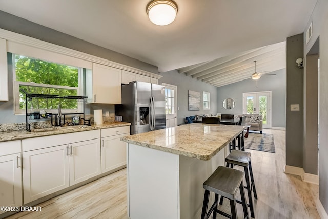 kitchen featuring vaulted ceiling with beams, ceiling fan, light stone counters, and stainless steel fridge with ice dispenser