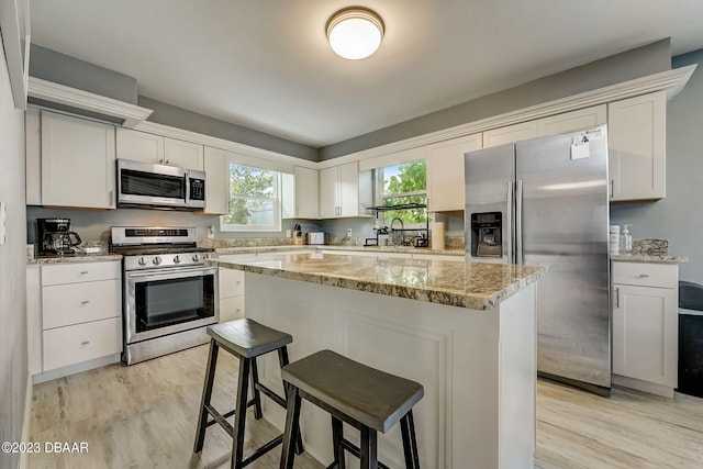 kitchen featuring a center island, stainless steel appliances, white cabinetry, and light hardwood / wood-style floors