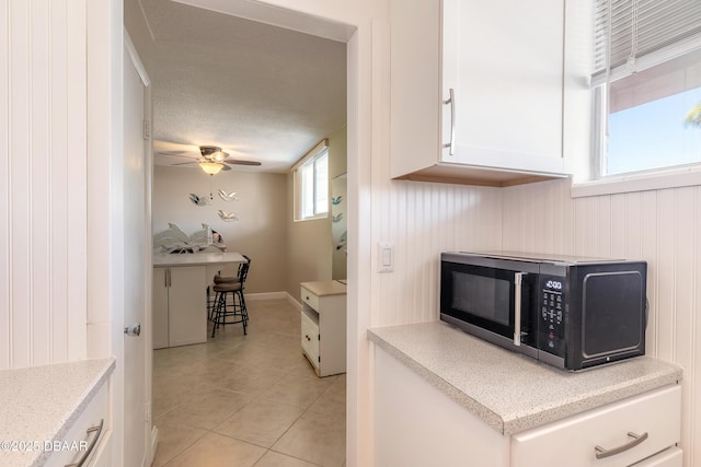 2727 N Atlantic Ave Unit 107, Daytona Beach, FL 32118 - kitchen with light tile patterned flooring, white cabinets, a ceiling fan, and light stone countertops