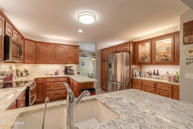 kitchen with tasteful backsplash, light stone counters, sink, and appliances with stainless steel finishes