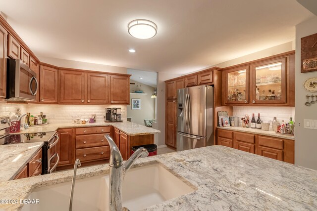 kitchen featuring decorative backsplash, stainless steel appliances, light stone counters, and sink