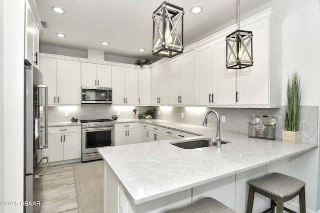 kitchen with hanging light fixtures, kitchen peninsula, appliances with stainless steel finishes, and white cabinetry