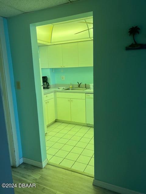 kitchen featuring sink, a drop ceiling, light tile patterned floors, white cabinets, and dishwasher