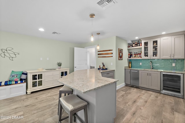 kitchen with wine cooler, gray cabinets, hanging light fixtures, a breakfast bar, and light hardwood / wood-style flooring