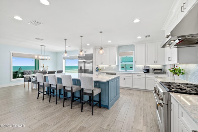 kitchen featuring white cabinetry, premium appliances, pendant lighting, a water view, and a center island