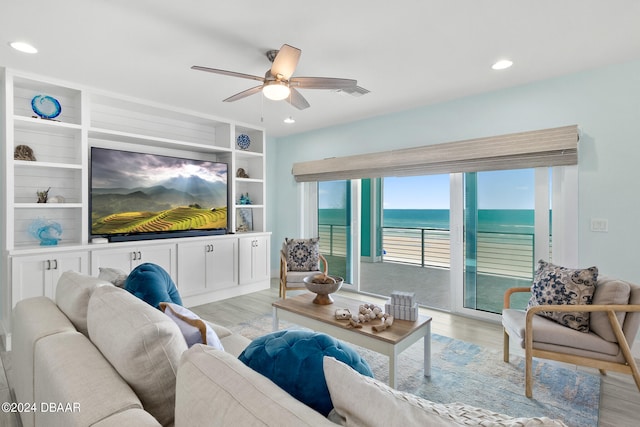 living room with built in shelves, ceiling fan, and light hardwood / wood-style flooring