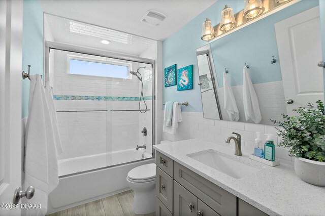 full bathroom with toilet, tile walls, bath / shower combo with glass door, hardwood / wood-style flooring, and vanity