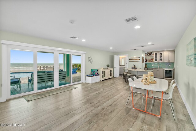 dining area featuring light hardwood / wood-style floors, bar, wine cooler, and a water view