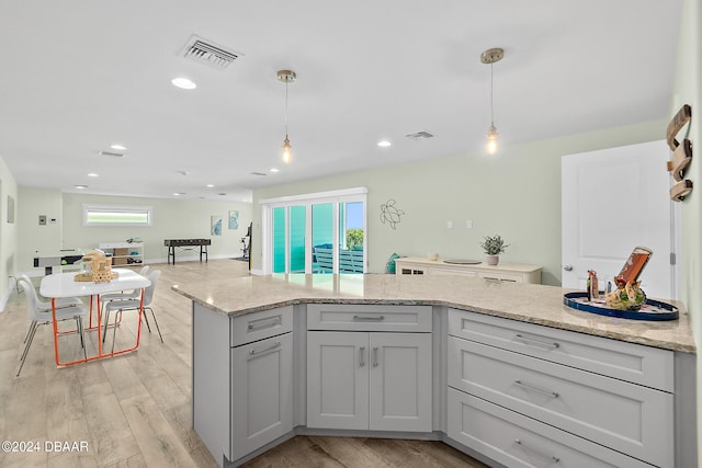 kitchen with light stone countertops, light hardwood / wood-style flooring, hanging light fixtures, and plenty of natural light