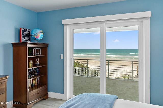 bedroom with light wood-type flooring, access to exterior, a beach view, and a water view