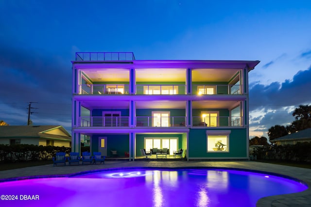 back house at dusk featuring a balcony and a patio