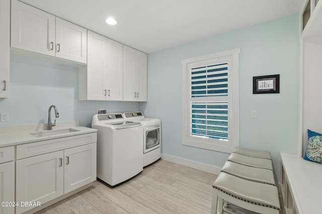 clothes washing area with cabinets, light hardwood / wood-style floors, washing machine and dryer, and sink