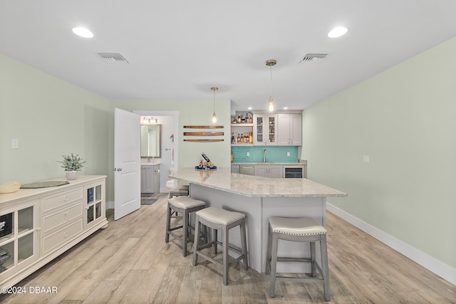 kitchen featuring a center island, light stone countertops, white cabinetry, light wood-type flooring, and decorative light fixtures