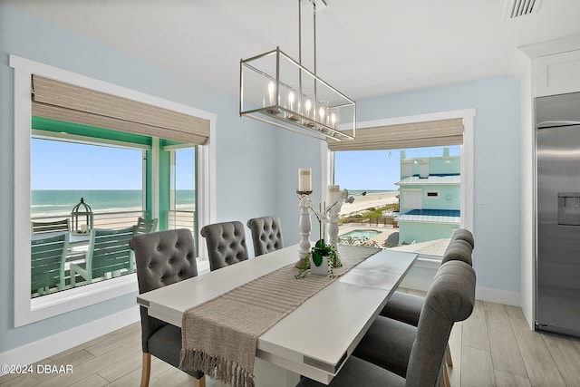 dining room with light wood-type flooring, a beach view, and a water view