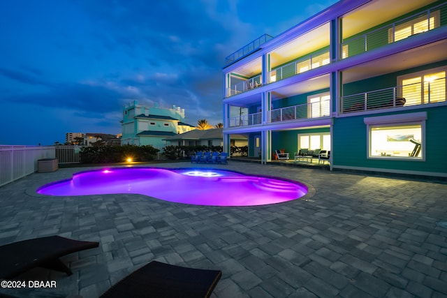 pool at dusk with a patio and an in ground hot tub