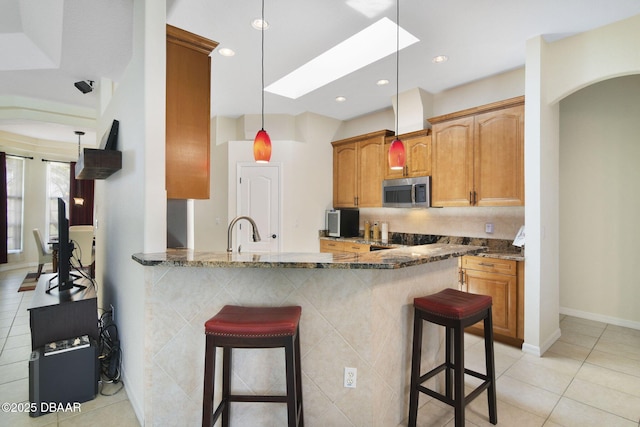2141 Springwater Ln, Port Orange, FL 32128 - kitchen featuring stainless steel microwave, a breakfast bar, dark stone counters, light tile patterned flooring, and a peninsula