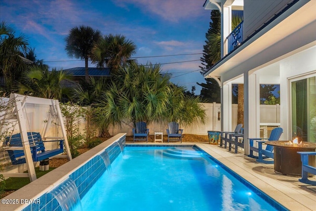 pool at dusk with a patio, pool water feature, and an outdoor fire pit