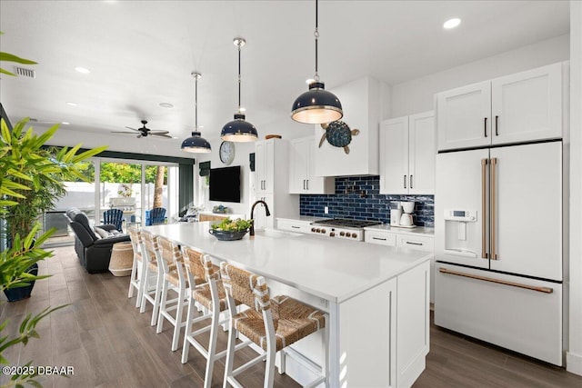 kitchen with high end white refrigerator, a center island with sink, a kitchen breakfast bar, white cabinets, and backsplash