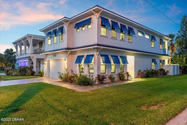 view of front of property featuring decorative driveway, an attached garage, a lawn, and stucco siding