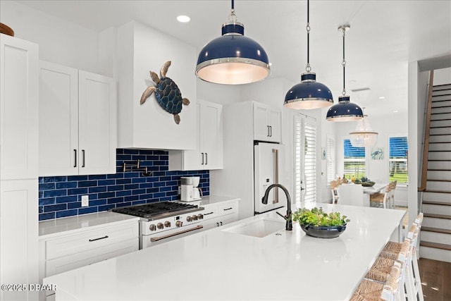 kitchen with backsplash, high end white fridge, gas range, an island with sink, and a sink