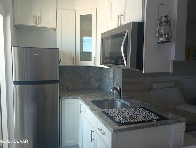 kitchen featuring glass insert cabinets, decorative backsplash, stainless steel appliances, white cabinetry, and a sink