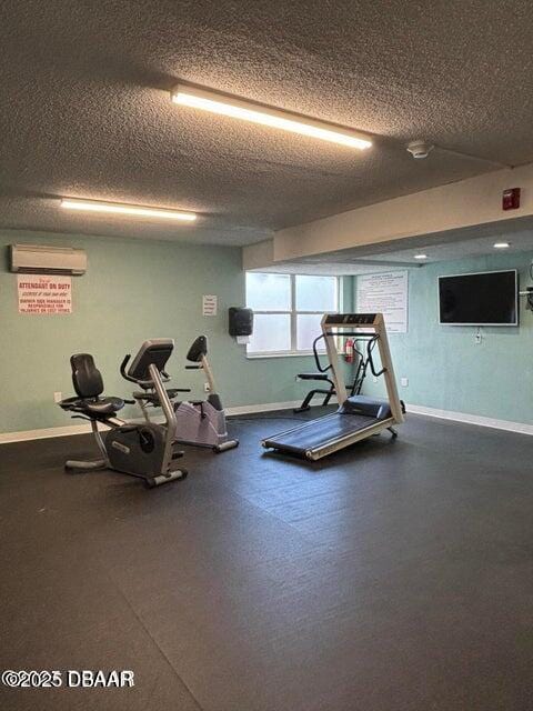 workout area featuring baseboards, a textured ceiling, and a wall unit AC