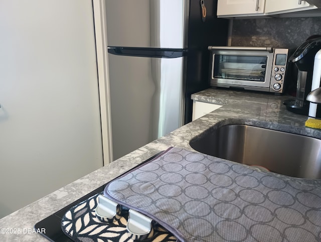 kitchen featuring dark stone counters, a toaster, freestanding refrigerator, decorative backsplash, and white cabinets