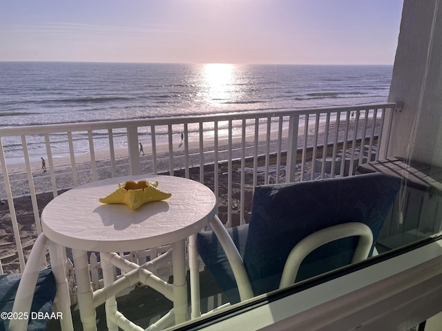 balcony at dusk featuring a beach view and a water view