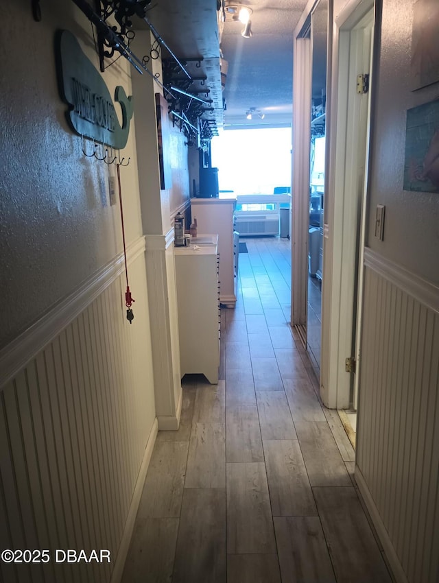 hall with wood finished floors and a wainscoted wall