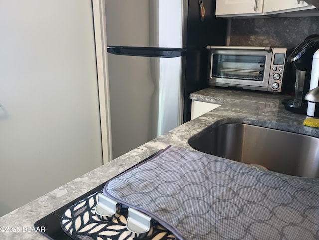 kitchen with dark stone counters, white cabinetry, a sink, freestanding refrigerator, and a toaster