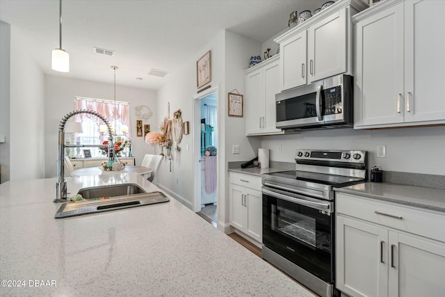 kitchen featuring appliances with stainless steel finishes, sink, pendant lighting, a notable chandelier, and white cabinets