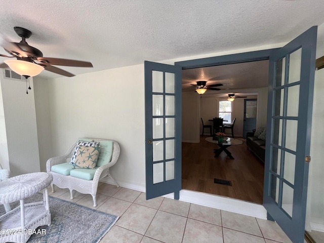 sitting room featuring ceiling fan, light wood-type flooring, a textured ceiling, and french doors