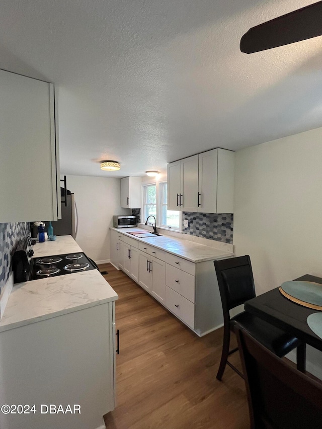 kitchen with decorative backsplash, sink, white cabinets, light hardwood / wood-style floors, and range with electric stovetop