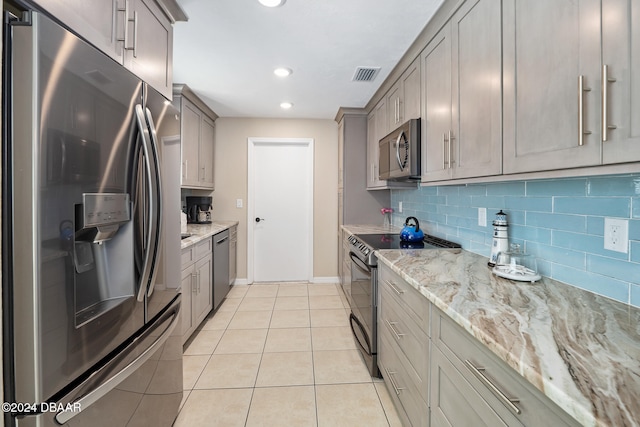 kitchen featuring tasteful backsplash, gray cabinetry, stainless steel appliances, light tile patterned floors, and light stone countertops