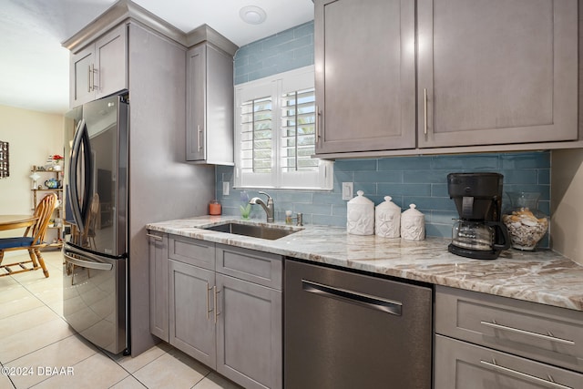 kitchen featuring sink, appliances with stainless steel finishes, tasteful backsplash, light stone countertops, and light tile patterned floors