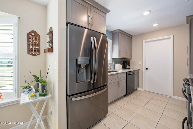 kitchen with light stone counters, light tile patterned flooring, backsplash, appliances with stainless steel finishes, and sink