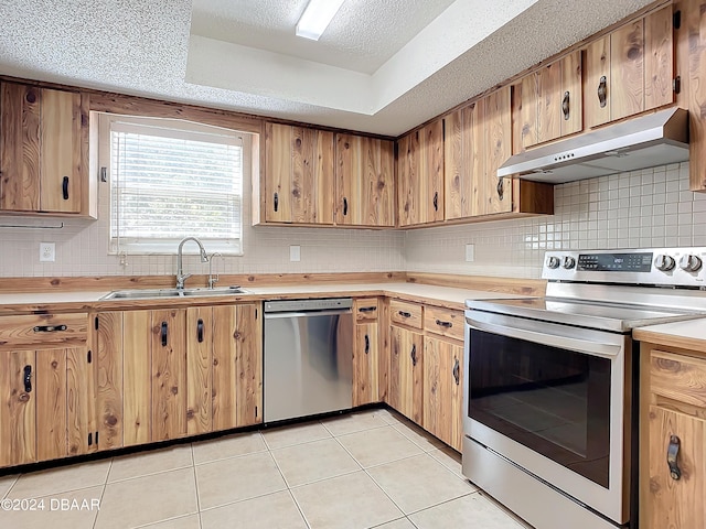 kitchen featuring sink, stainless steel appliances, a textured ceiling, a tray ceiling, and light tile patterned floors