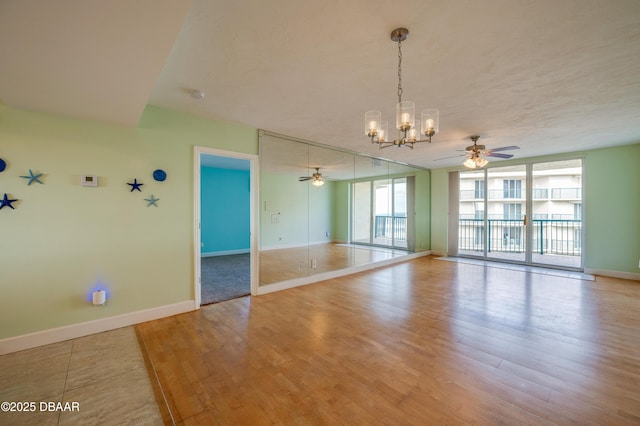 empty room featuring ceiling fan with notable chandelier, expansive windows, and light wood-type flooring