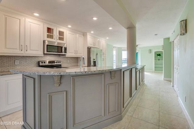 kitchen featuring light tile patterned floors, an island with sink, ceiling fan, stainless steel appliances, and white cabinets