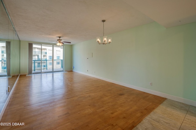 spare room with light wood-type flooring, ceiling fan with notable chandelier, and expansive windows