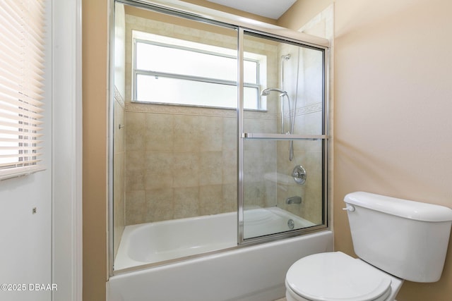 bathroom featuring toilet and shower / bath combination with glass door