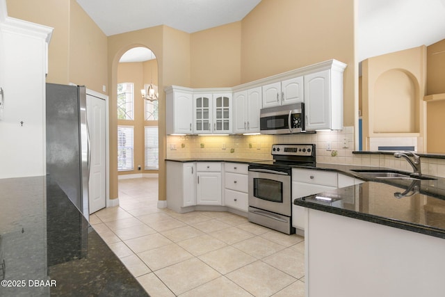 kitchen featuring a high ceiling, light tile patterned flooring, a sink, appliances with stainless steel finishes, and tasteful backsplash